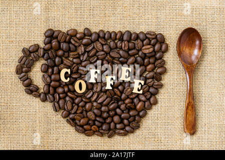 Caffè torrefatto in grani a forma di tazza di close-up con la parola caffè e cucchiaio di legno su tela naturale, il sacco Foto Stock