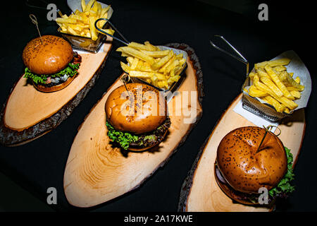 Una porzione tripla di hamburger di manzo servita con patate fritte su un di legno tronco di albero piatto Foto Stock