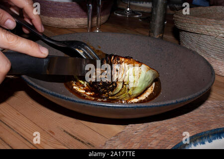 Le mani della persona con coltello e forchetta taglio cavolo bruciato cucina in stile gourmet Foto Stock