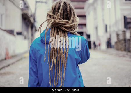 Giovane uomo per le strade con lunghi dreadlocks utilizzando giacca blu Foto Stock