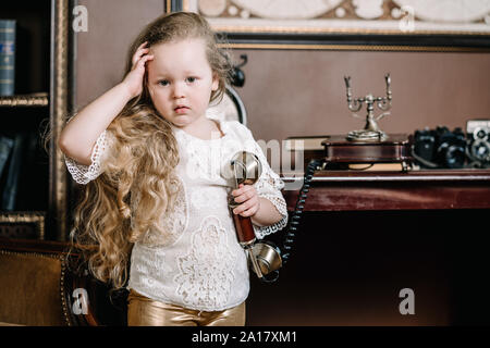 Poco meditabondo bambino ragazza a parlare su un telefono retrò in camera da soli con una triste emozioni. Foto Stock