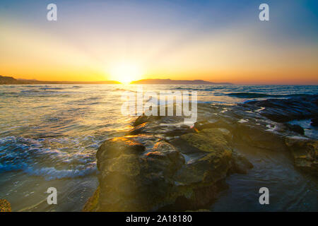 Un nuovo inizio e una nuova speranza con i raggi del sole che sorge dal mare all'orizzonte. Foto Stock