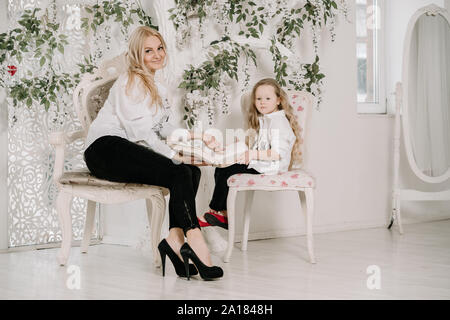 Ritratto di Madre e figlia in interni felice seduta vicino e la lettura di libri insieme in ambienti chiusi in camera bianca. Foto Stock