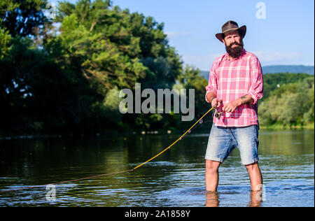 Fly fish hobby. Estate attività alieutiche. pescatore in acqua di lago. hipster pesca con cucchiaio-esca. Big game pesca. Rilassatevi sulla natura. maturo uomo barbuto con pesce sull'asta. Egli è pronto per la pesca. Foto Stock