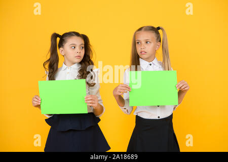 Riflettendo su un lavoro a casa. Figlioli holding fogli vuoti per esame lavoro su sfondo giallo. Le piccole bambine con vuoto libri verdi per il lavoro di progetto o di ricerca. La carta funziona, copiare lo spazio. Foto Stock