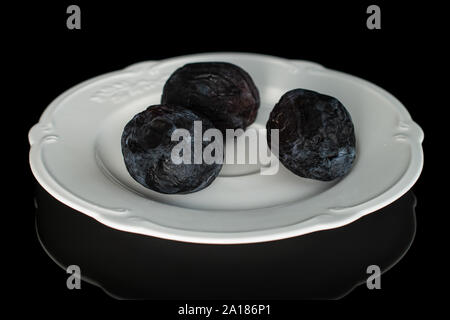 Gruppo di tre tutta la essiccazione blu scuro prugna sulla piastra bianca isolata su vetro nero Foto Stock