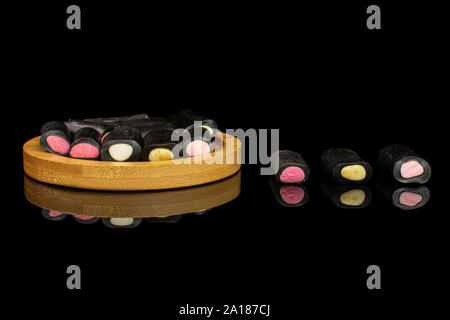 Sacco di tutto il dolce di liquirizia nera caramella sul bambù coaster isolato sul vetro nero Foto Stock