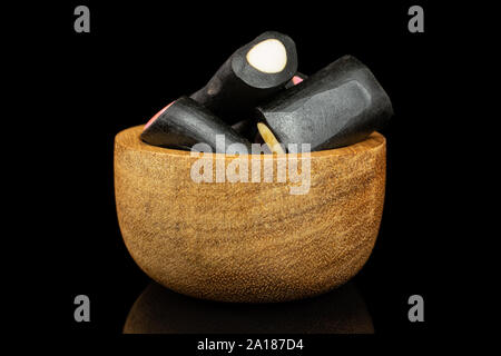 Sacco di tutto il dolce di liquirizia nera candy in piccola ciotola di legno isolata sul vetro nero Foto Stock