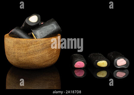 Sacco di tutto il dolce di liquirizia nera candy in piccola ciotola di legno isolata sul vetro nero Foto Stock