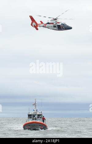 Un Coast Guard MH-65 Delfino elicottero vola al di sopra di una guardia costiera di 45 piedi barca risposta-mezzo vicino a Brooklyn, New York, 14 maggio 2019. Missioni di formazione tra una piccola barca station equipaggi e stazione aria gli equipaggi si verificano regolarmente per mantenere i deputati pronti a rispondere quando i marinai sono in pericolo. (U.S. Coast Guard foto di Sottufficiali di 2a classe di Steve Strohmaier) Foto Stock