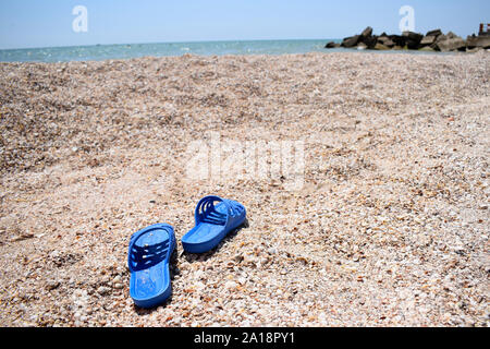 Estate pantofole sulla spiaggia vicino all'acqua. Conchiglie di mare in una giornata di sole. Tropical Beach vacanza e concetto di viaggio Foto Stock