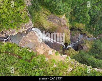 Antenna vista superiore della coppia di viaggio salutando drone, in piedi sul bordo di 500 piedi cascata nell'isola tropicale giungla del Black River Gorges Foto Stock