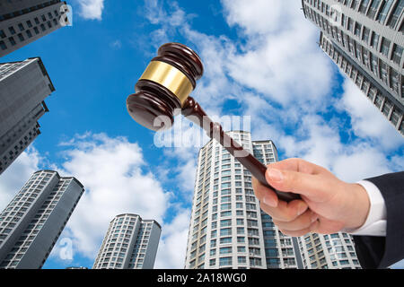 La mano di un imprenditore tenendo un giudice martello sulla costruzione dello sfondo. Asta o concetto di fallimento. Foto Stock