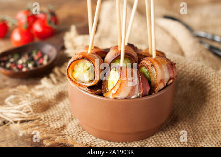 Pancetta avvolto Il cavoletto di Bruxelles è servita con pomodorini in vaso in ceramica. Antipasto rotoli Foto Stock