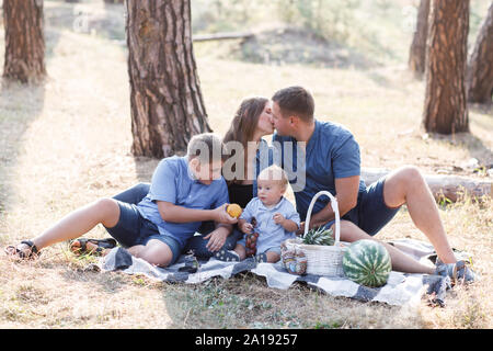 Bella famiglia felice - i genitori e i due figli, il trascorrere del tempo nella natura, ridendo, mangiare frutta fresca Foto Stock