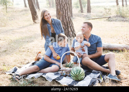 Bella famiglia felice - i genitori e i due figli, il trascorrere del tempo nella natura, ridendo, mangiare frutta fresca Foto Stock