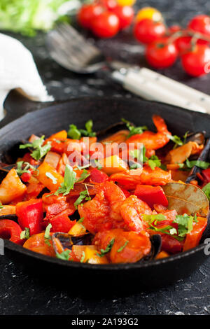 Stufato di pesce cioppino con gamberetti, capesante, vongole, cozze e pesce in padella sulla tavola nera, servita con verdure Foto Stock