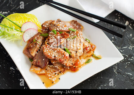 Stir-maiale fritto con kimchi servito con semi di sesamo e cipolla tritata sulla tavola nera Foto Stock