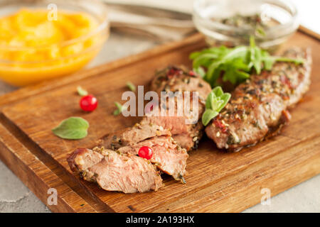 Agnello arrosto di filetto con crosta piccante, mirtilli e foglie di salvia sul tagliere di legno Foto Stock