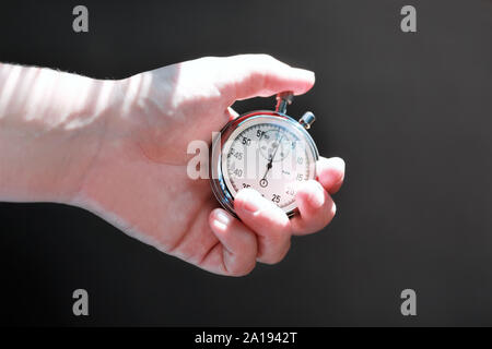 Mano che tiene un cronometro e premendo il pulsante per tenere il tempo. Sfondo scuro Foto Stock