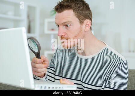 Utilizzando una lente di ingrandimento per leggere qualcosa in internet Foto Stock