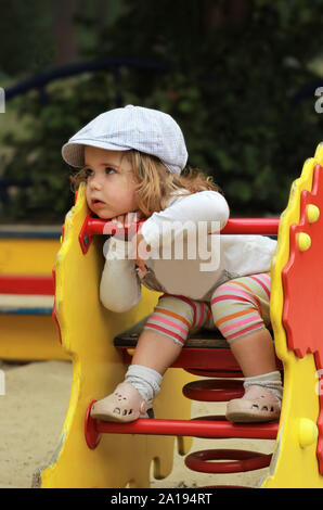 Considerato elegante un anno vecchio ragazza in un cappuccio controllati seduto su un parco giochi Foto Stock