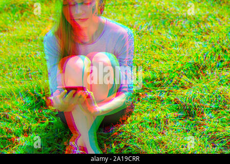 Effetto di glitch. Giovane bella ragazza seduta sul prato di parco guardando al telefono cellulare. Copia banner space Foto Stock