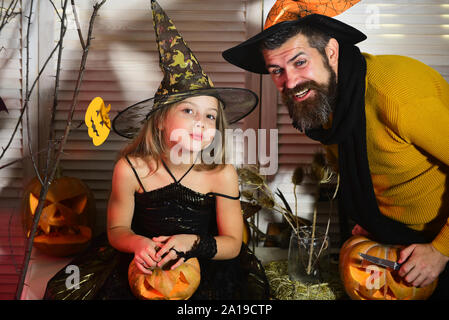 Padre e figlia con decorazioni di Halloween. Festa di Halloween concetto. Procedura guidata e poco strega in cappelli tenere le zucche. Ragazza e uomo barbuto con un sorridente Foto Stock