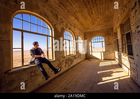 Tourist si siede in una vedova di una casa in rovina in Kolmanskop città fantasma, Namibia Foto Stock