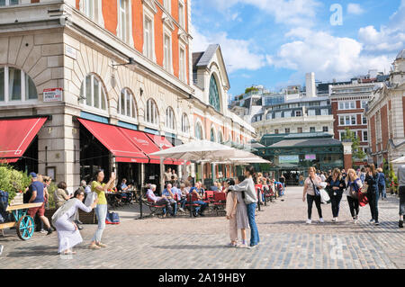 Turisti che si godono il clima estivo al Covent Garden Piazza nel West End di Londra, London, England, Regno Unito Foto Stock