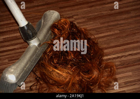 Qualcuno rosso di spazzamento ritagli di capelli sul pavimento close-up, parrucchiere spazzare il pavimento in legno dopo il taglio di capelli in un salone di parrucchiere Foto Stock