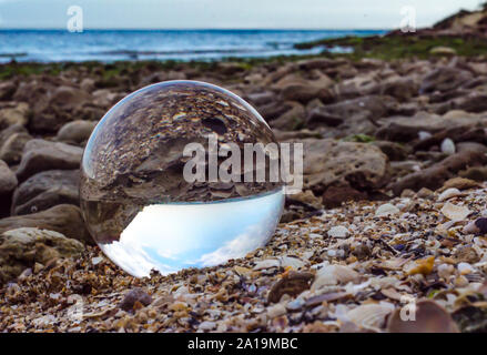 Vetro in cristallo lente a sfera giace sulla sabbia di mare paesaggio Foto Stock