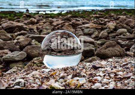 Vetro in cristallo lente a sfera giace sulla sabbia del mare Foto Stock