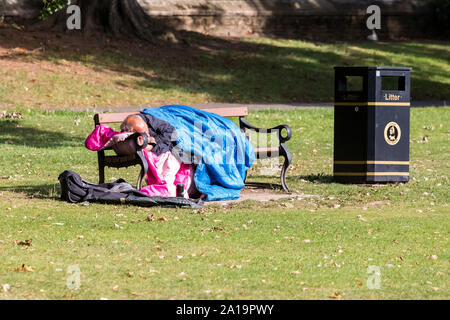 Senzatetto uomo addormentato nel suo sacco a pelo su una panchina nel parco Foto Stock