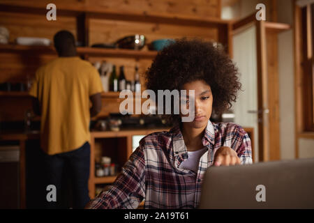 Giovane donna utilizzando computer portatile in una cucina Foto Stock