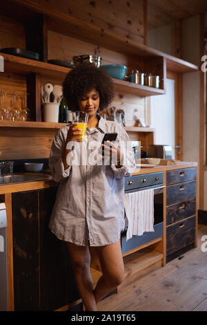 Giovane donna utilizza lo smartphone in cucina Foto Stock