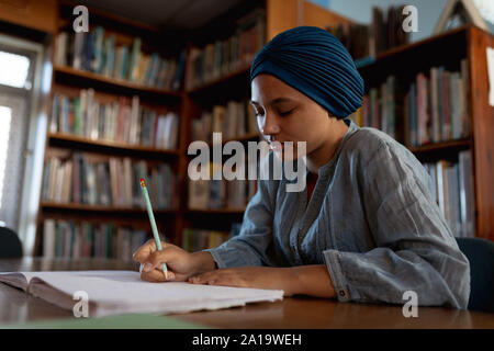 Giovane donna studiare in biblioteca Foto Stock