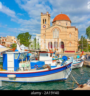 Fshing barche e waterfront con Ekklisia Isodia Theotokou chiesa sulla soleggiata giornata estiva nella città di Egina, Isole Saroniche, Grecia Foto Stock