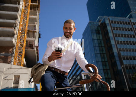 Giovani professionisti uomo seduto su una bicicletta utilizzando smartphone su strada Foto Stock