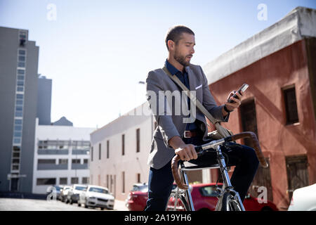 Giovane uomo professionale utilizzando lo smartphone e seduta sulla moto Foto Stock