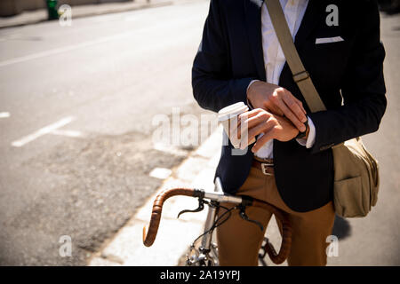Giovane uomo professionale controllo tempo e seduto su una bicicletta Foto Stock