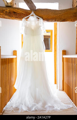 Un spose abito da sposa appeso a una quercia trave di legno sul pianerottolo Foto Stock