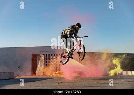 BMX rider su un tetto di salto e usando granate fumogene Foto Stock