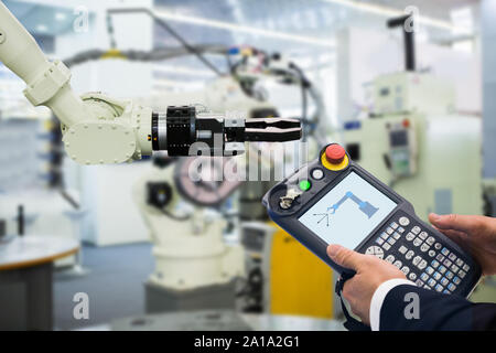 Ingegnere con teach pendant dispositivo. Programmazione di robot con braccio robotico. Smart factory Foto Stock