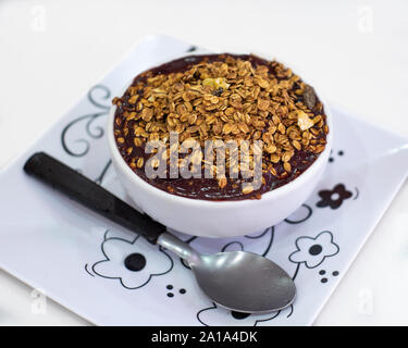 Una ciotola di Acai berry con granola sulla piastra bianca isolata su sfondo bianco visto da un angolo con un cucchiaio Foto Stock