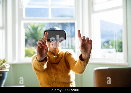 Donna matura da soli a casa in cuffia VR Foto Stock