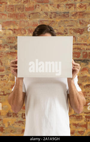 Tela vuota tenuto di fronte a un muro di mattoni Foto Stock