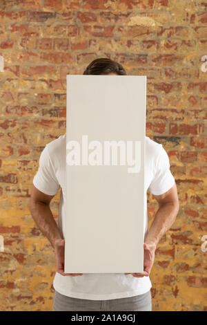 Tela vuota tenuto di fronte a un muro di mattoni Foto Stock