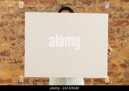 Tela vuota tenuto di fronte a un muro di mattoni Foto Stock