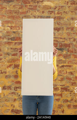 Tela vuota tenuto di fronte a un muro di mattoni Foto Stock